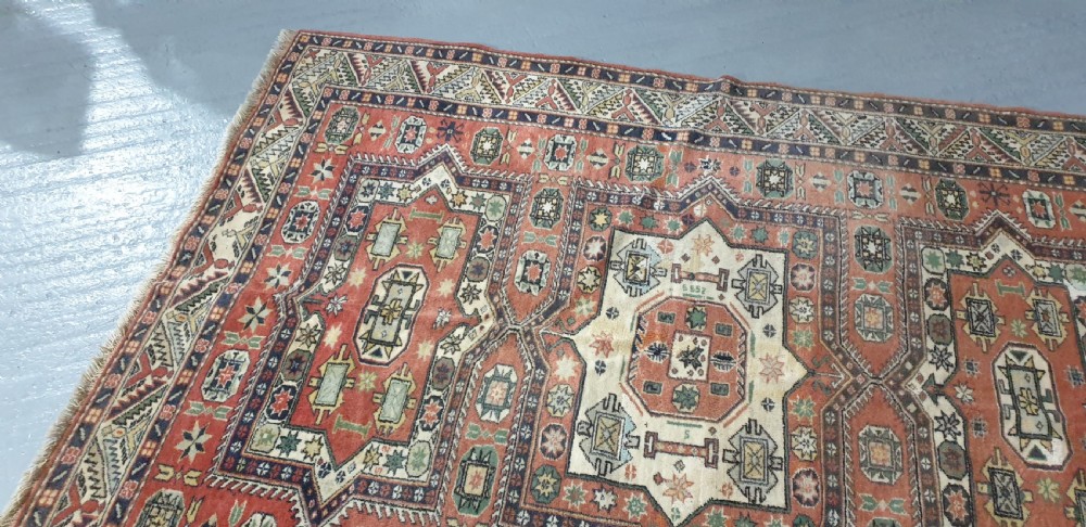 A large hand-knotted Persian wool area rug featuring central geometric medallions in terracotta red, navy blue, green, and cream. View VII