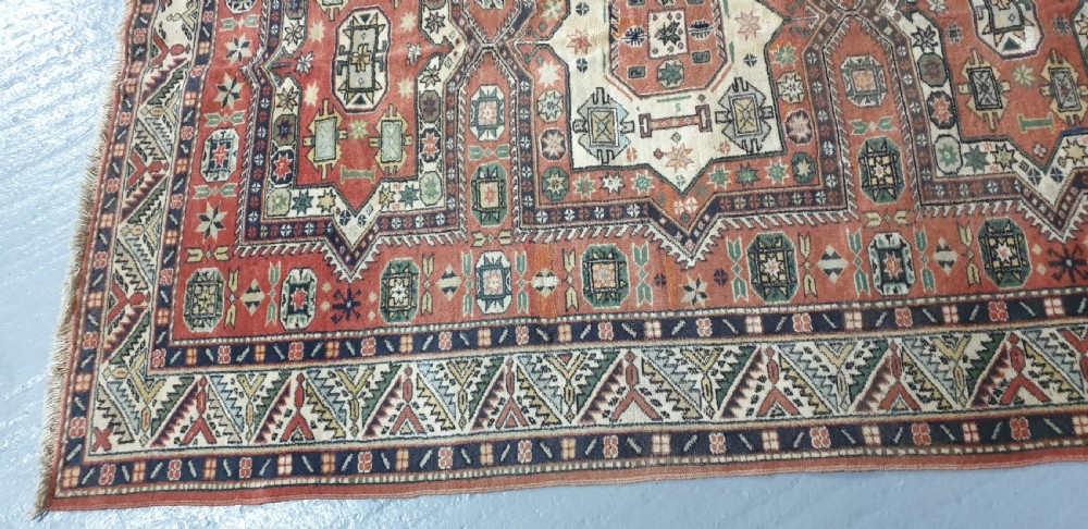 A large hand-knotted Persian wool area rug featuring central geometric medallions in terracotta red, navy blue, green, and cream. View IX