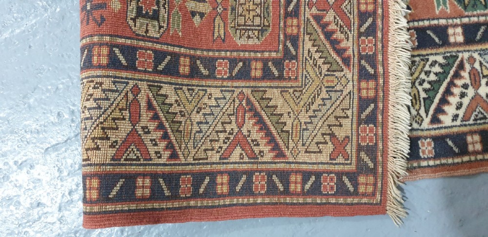 A large hand-knotted Persian wool area rug featuring central geometric medallions in terracotta red, navy blue, green, and cream. View X