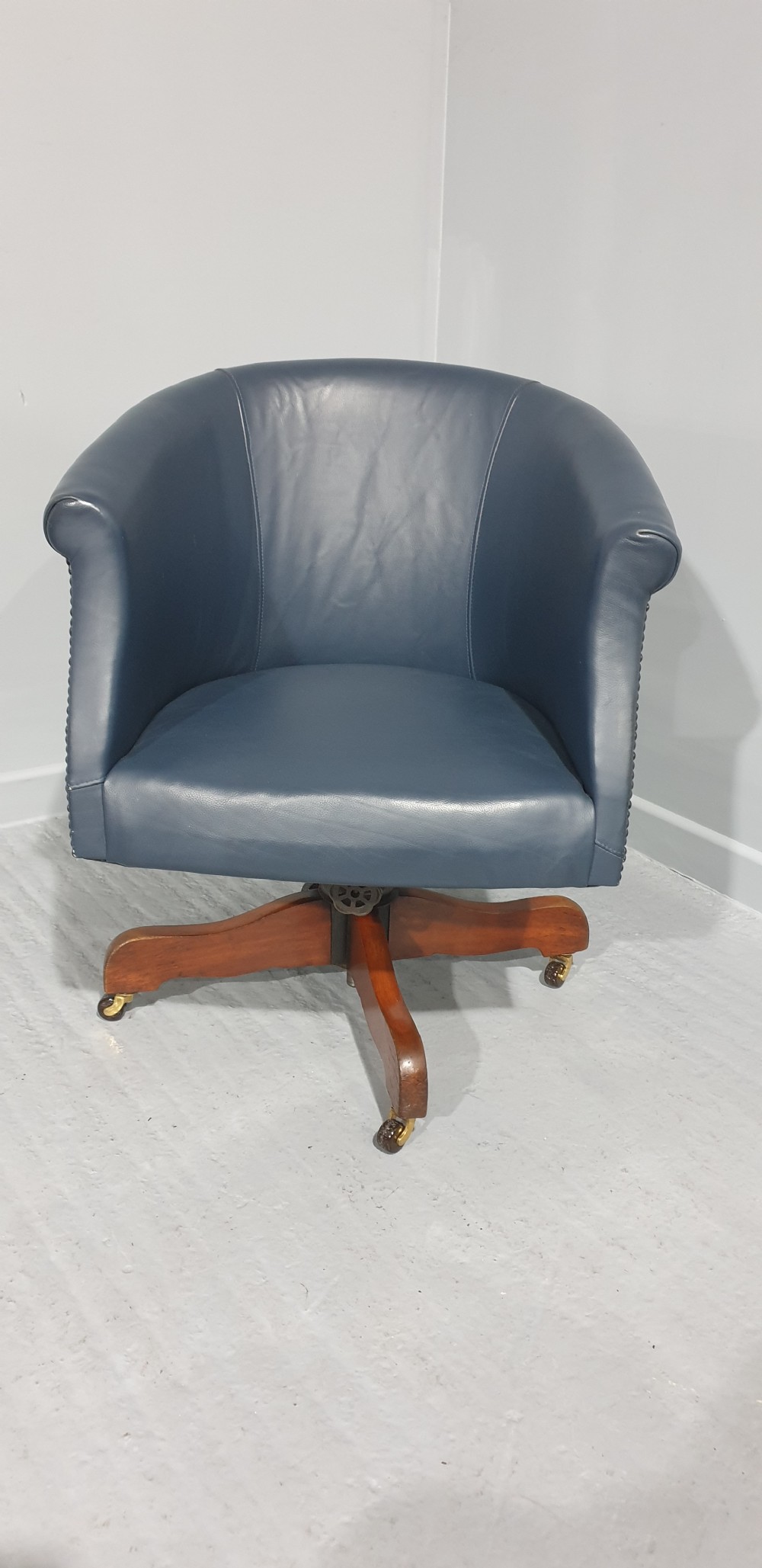 A blue leather tub desk chair with a curved backrest, brass studding detail, and a swivel wood quadruped base on castors. View II