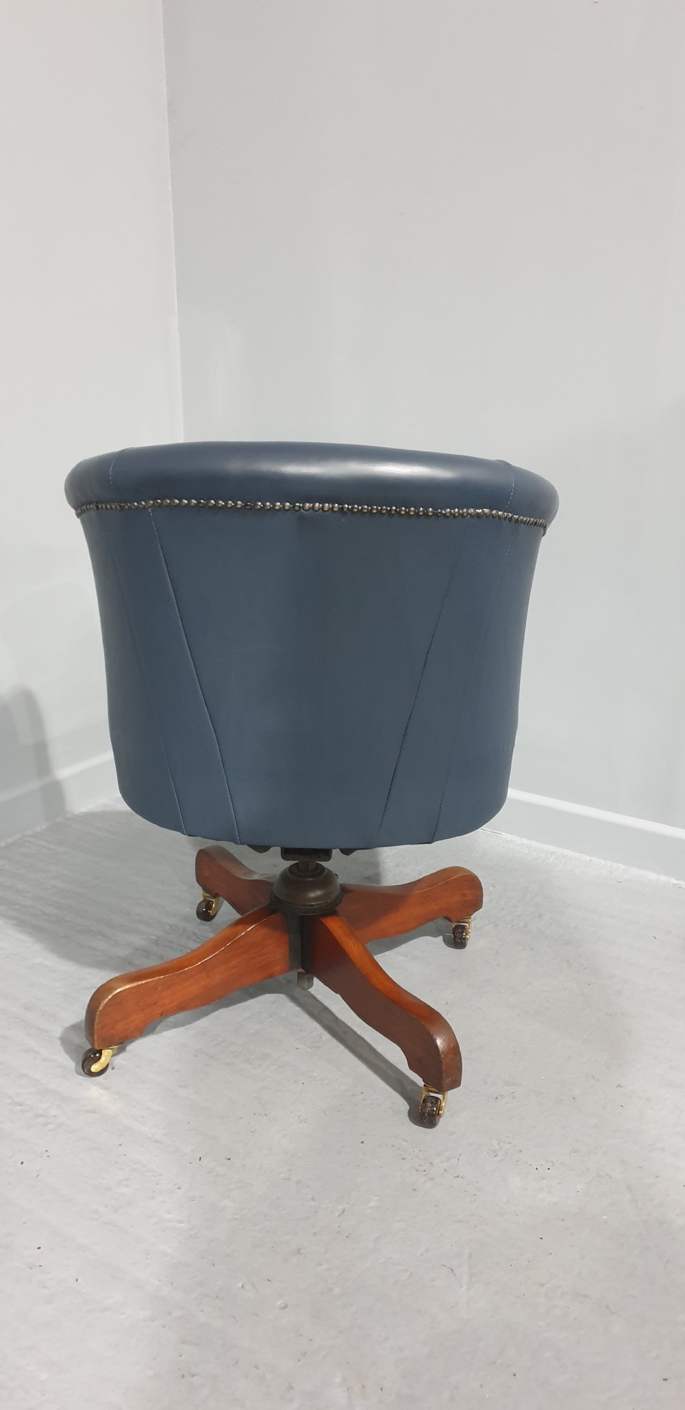 A blue leather tub desk chair with a curved backrest, brass studding detail, and a swivel wood quadruped base on castors. View III