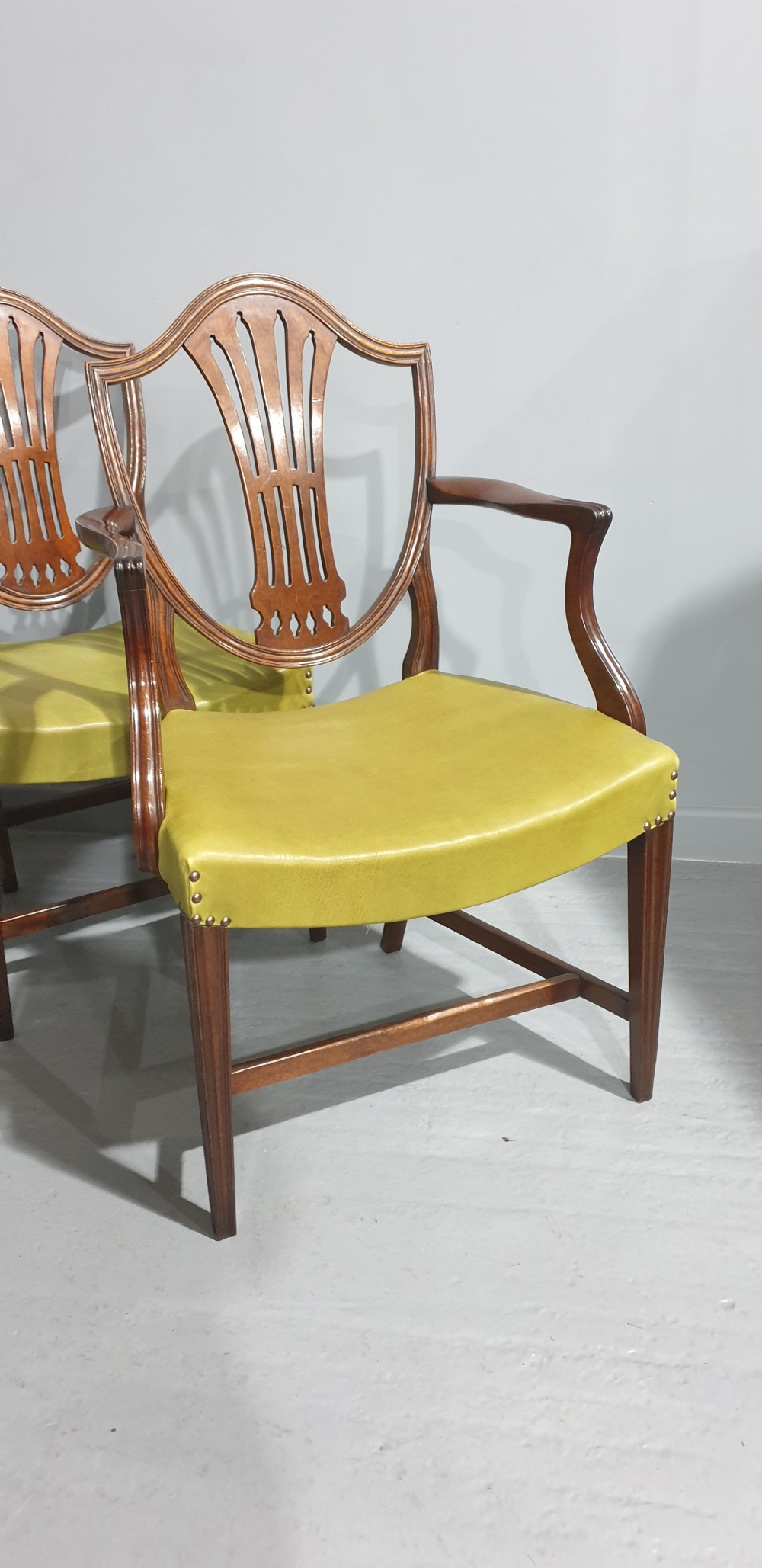 A set of six Georgian mahogany shield-back dining chairs, including two carvers and four side chairs, featuring yellow-green leather seats with brass studding. View V