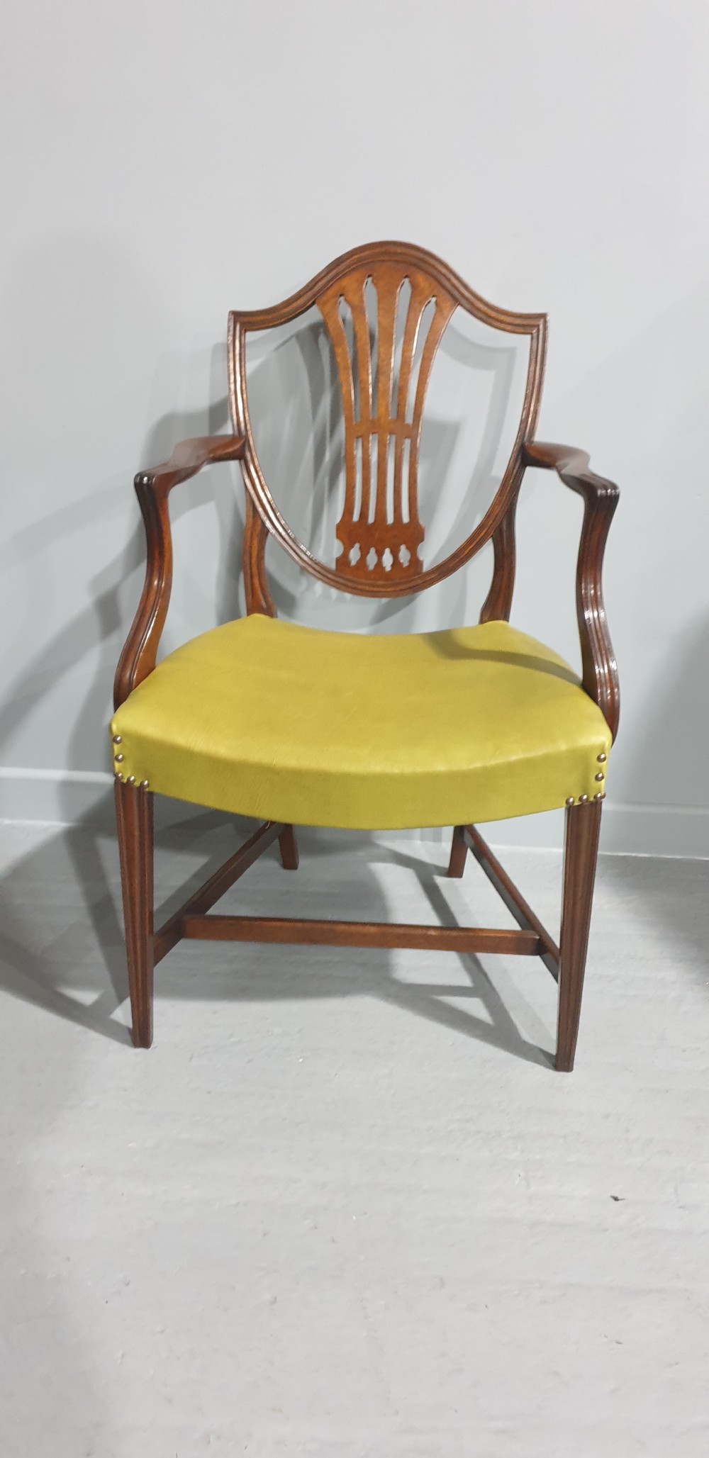 A set of six Georgian mahogany shield-back dining chairs, including two carvers and four side chairs, featuring yellow-green leather seats with brass studding. View VI