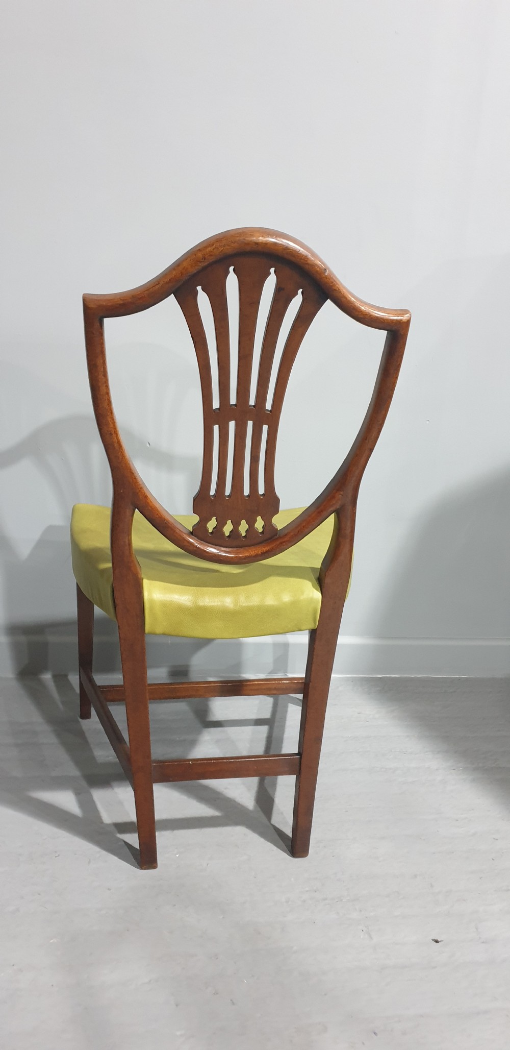 A set of six Georgian mahogany shield-back dining chairs, including two carvers and four side chairs, featuring yellow-green leather seats with brass studding. View VII