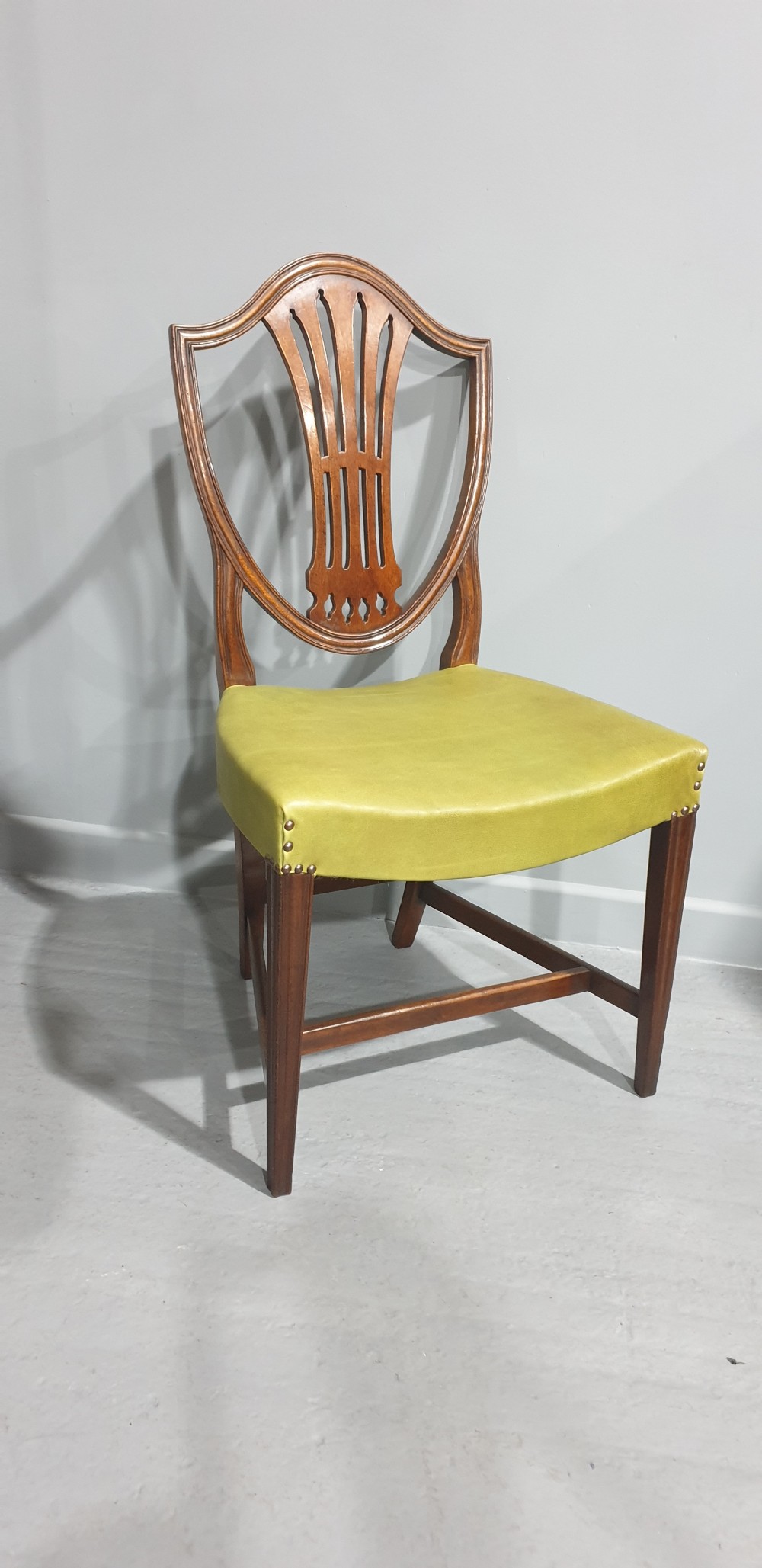 A set of six Georgian mahogany shield-back dining chairs, including two carvers and four side chairs, featuring yellow-green leather seats with brass studding. View X