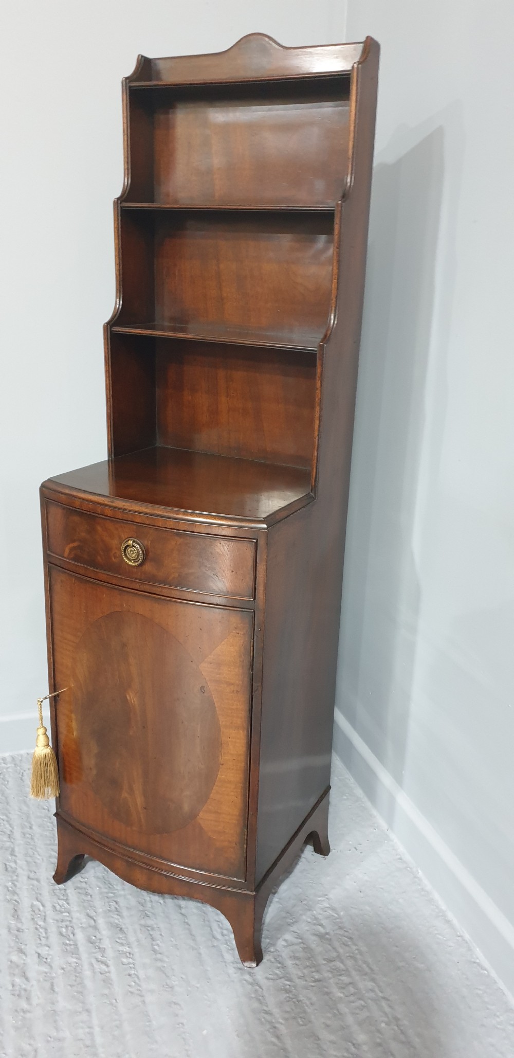 A tall, narrow mahogany cabinet featuring three open graduated shelves above a single drawer and a lower cupboard door with an oval flame mahogany inlay. View II