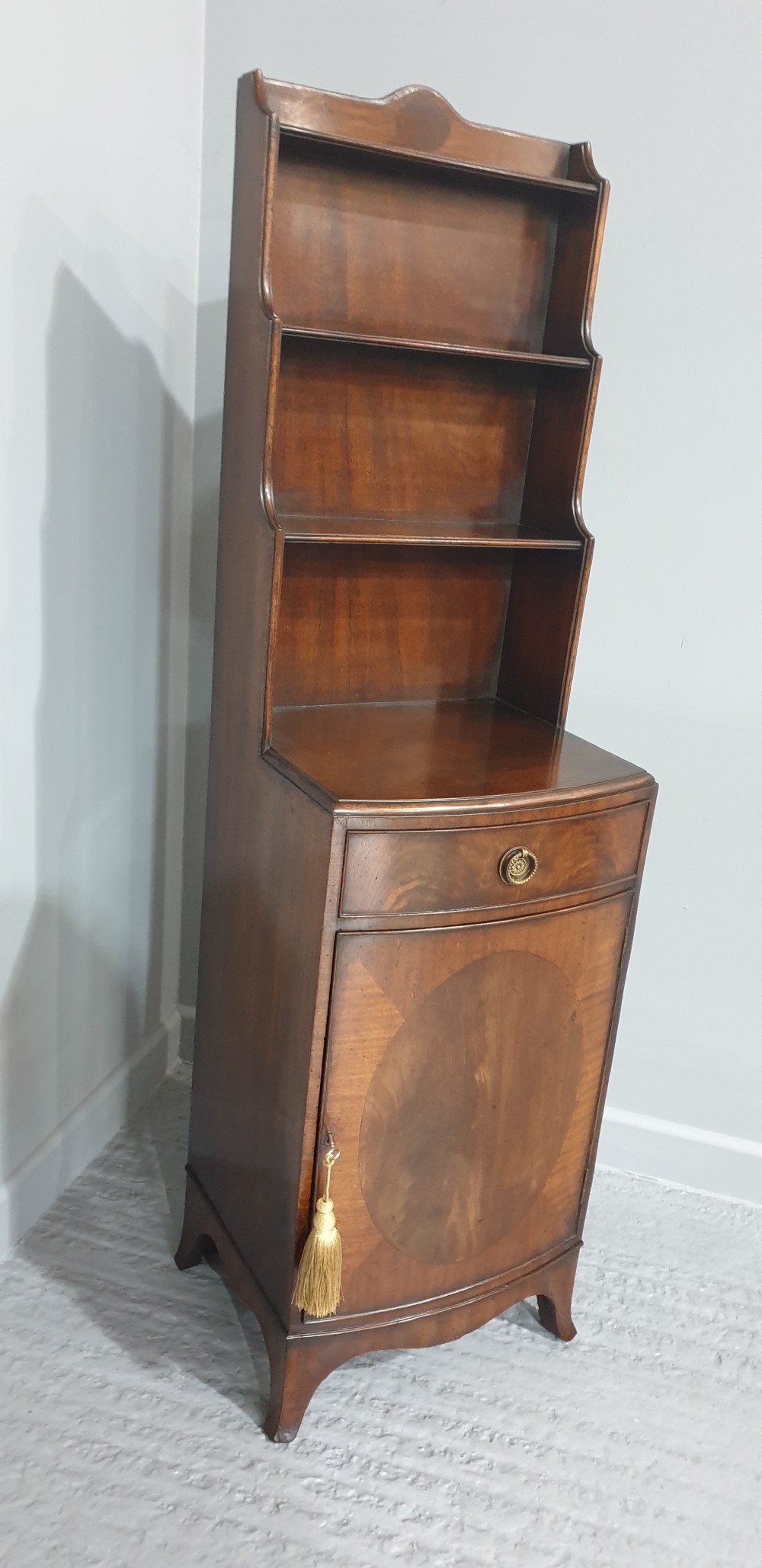 A tall, narrow mahogany cabinet featuring three open graduated shelves above a single drawer and a lower cupboard door with an oval flame mahogany inlay. View III