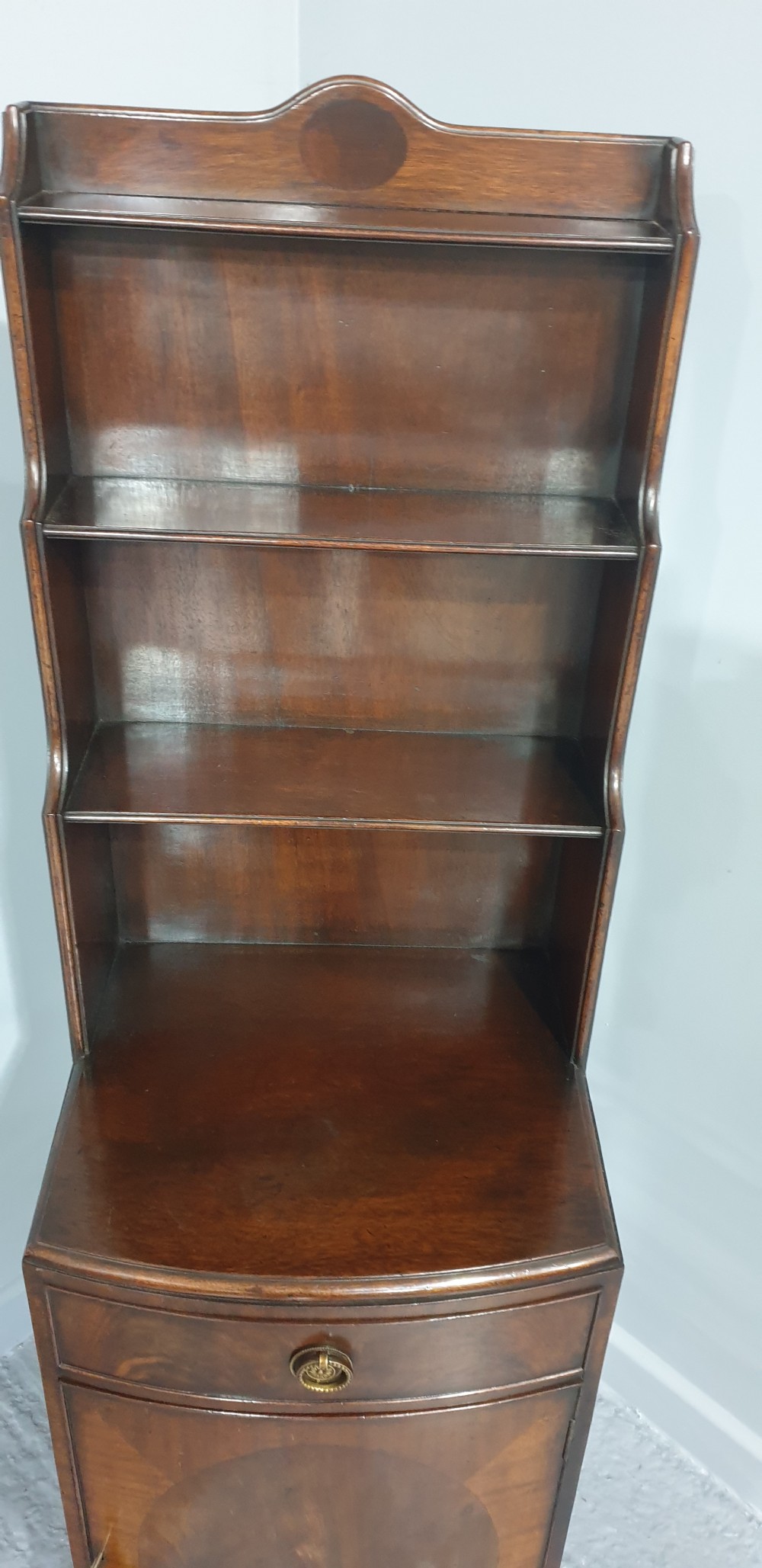 A tall, narrow mahogany cabinet featuring three open graduated shelves above a single drawer and a lower cupboard door with an oval flame mahogany inlay. View V