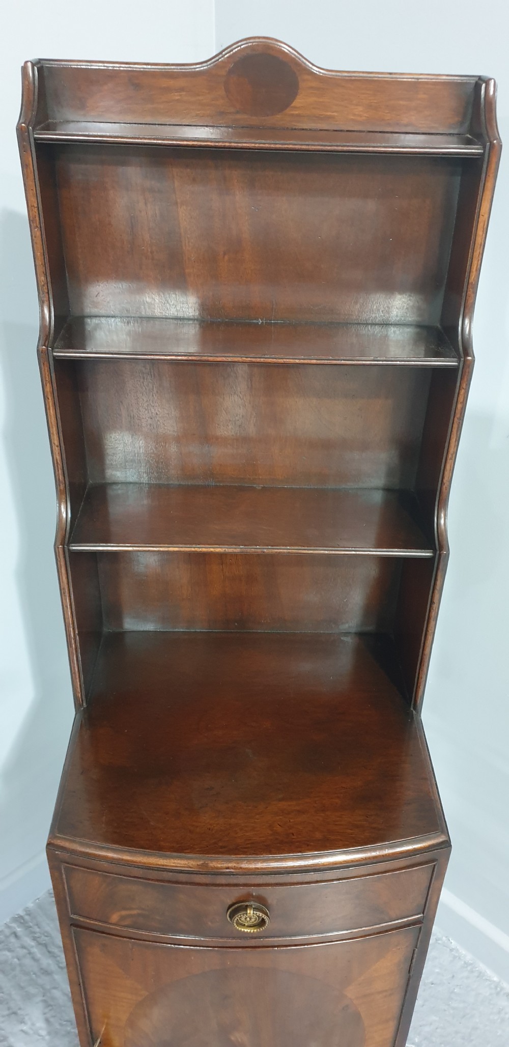 A tall, narrow mahogany cabinet featuring three open graduated shelves above a single drawer and a lower cupboard door with an oval flame mahogany inlay. View VI