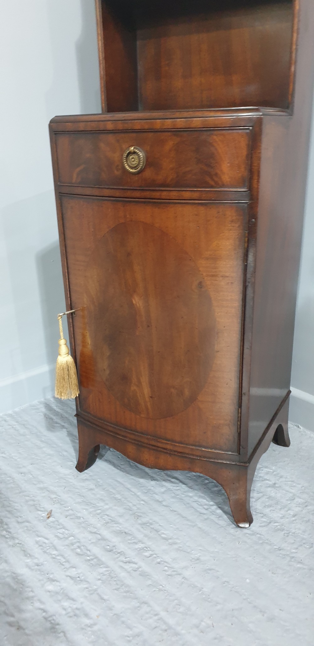 A tall, narrow mahogany cabinet featuring three open graduated shelves above a single drawer and a lower cupboard door with an oval flame mahogany inlay. View IX