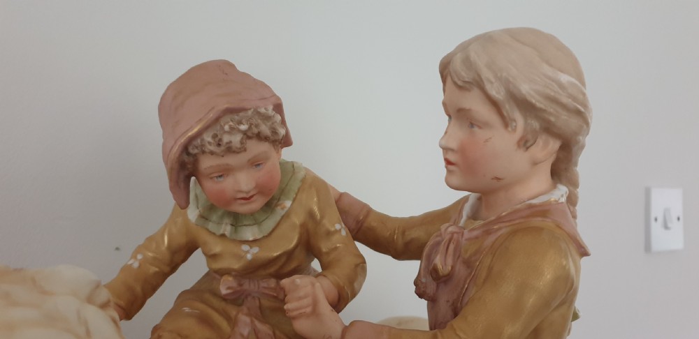 An antique Royal Dux porcelain figure group depicting two children interacting with a large dog on a green base. View III
