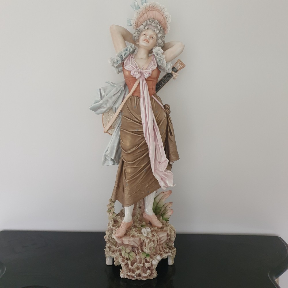 A tall Royal Dux porcelain figure of a lady in historical attire holding a musical instrument on an ornate base.