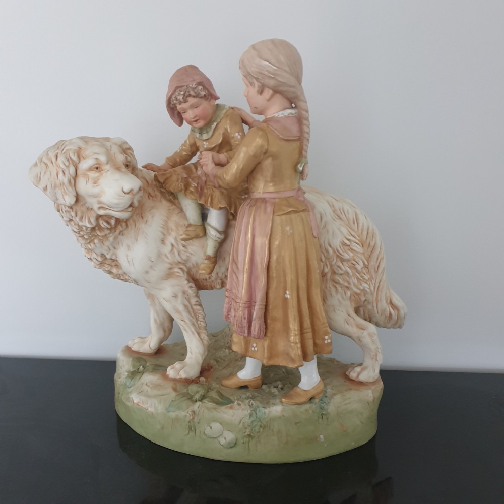 An antique Royal Dux porcelain figure group depicting two children interacting with a large dog on a green base.