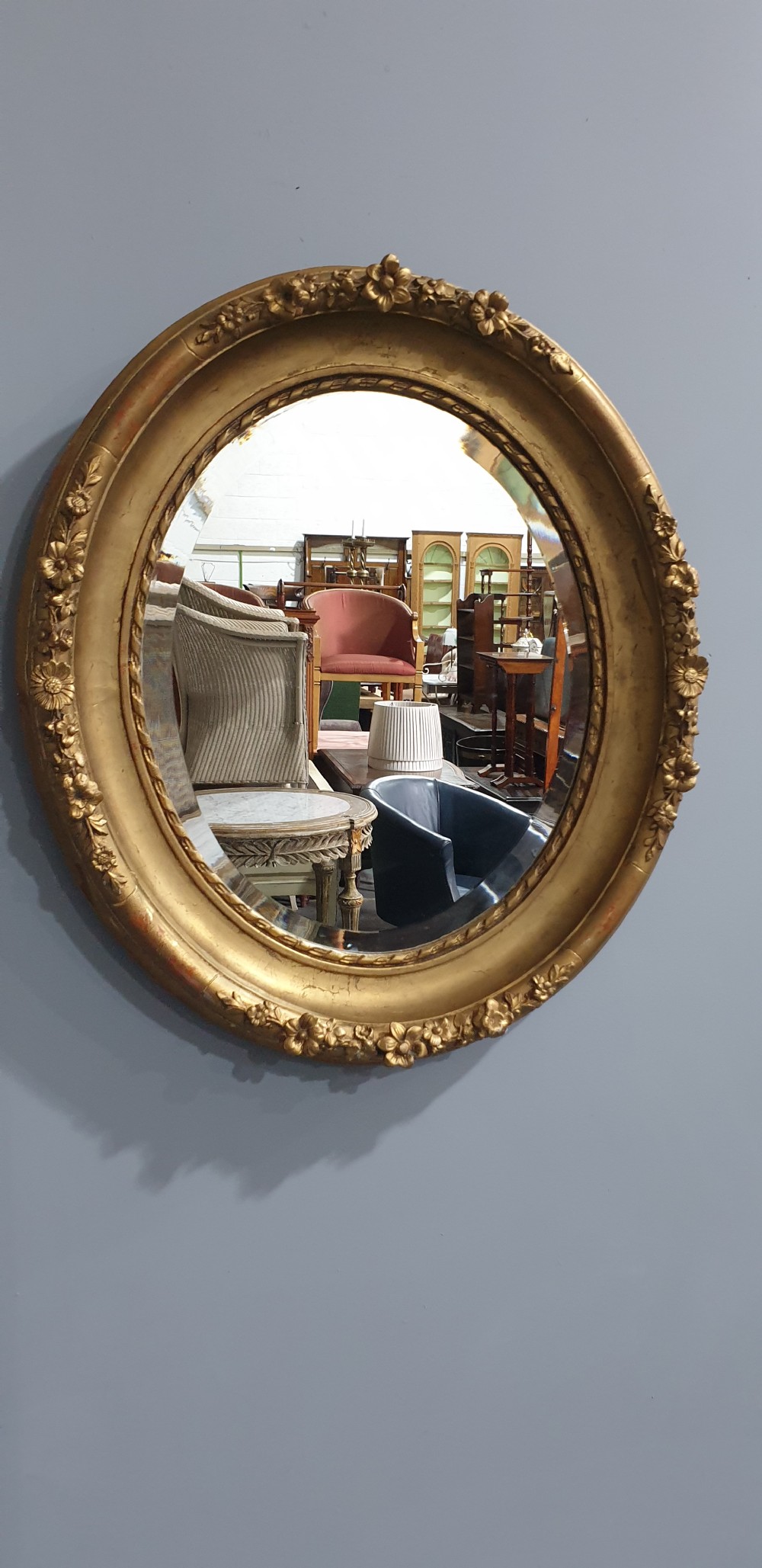 An oval Victorian wall mirror featuring a giltwood frame decorated with a floral motif outer border and a inner rope twist moulding. View II