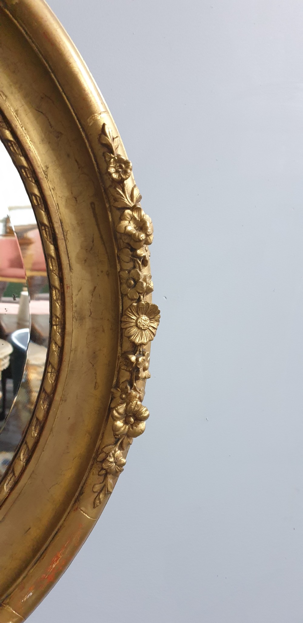 An oval Victorian wall mirror featuring a giltwood frame decorated with a floral motif outer border and a inner rope twist moulding. View IV