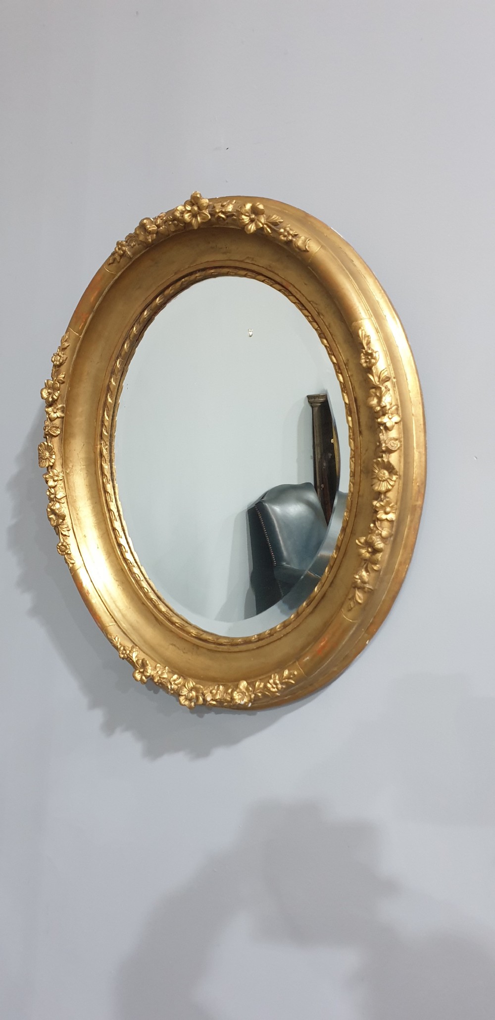 An oval Victorian wall mirror featuring a giltwood frame decorated with a floral motif outer border and a inner rope twist moulding. View VI