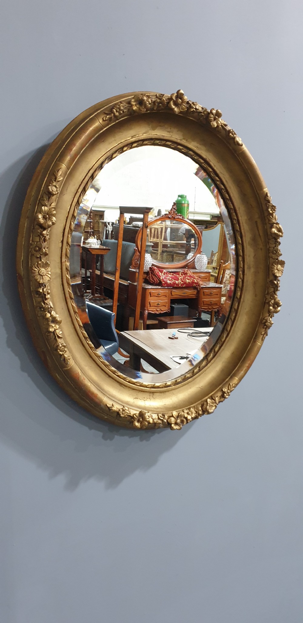 An oval Victorian wall mirror featuring a giltwood frame decorated with a floral motif outer border and a inner rope twist moulding. View VII