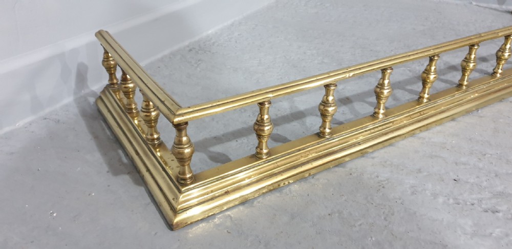 A low Regency style polished brass fireplace fender featuring turned baluster spindles along a moulded base. View IV
