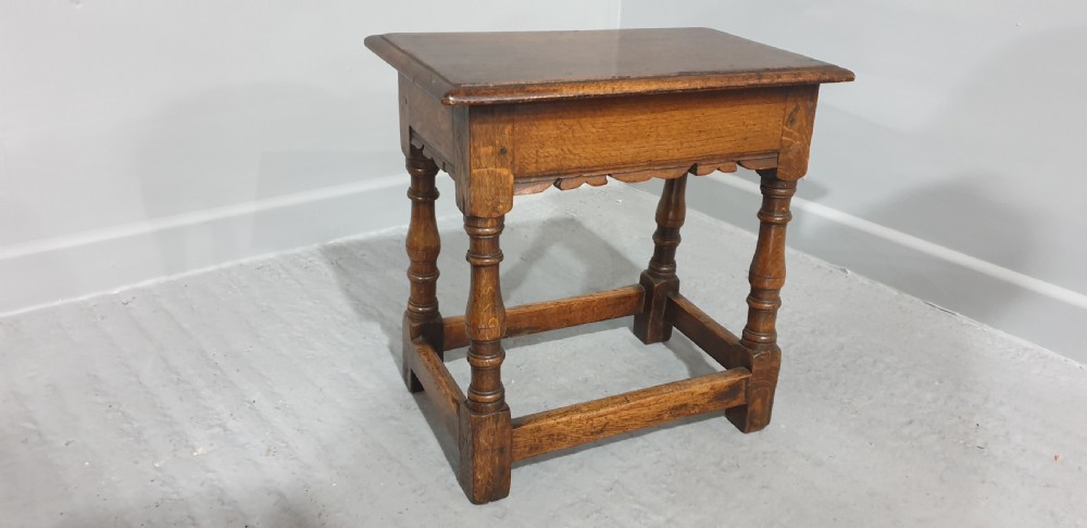A rectangular oak joint stool featuring turned legs, a shaped apron, and perimeter box stretchers. View II