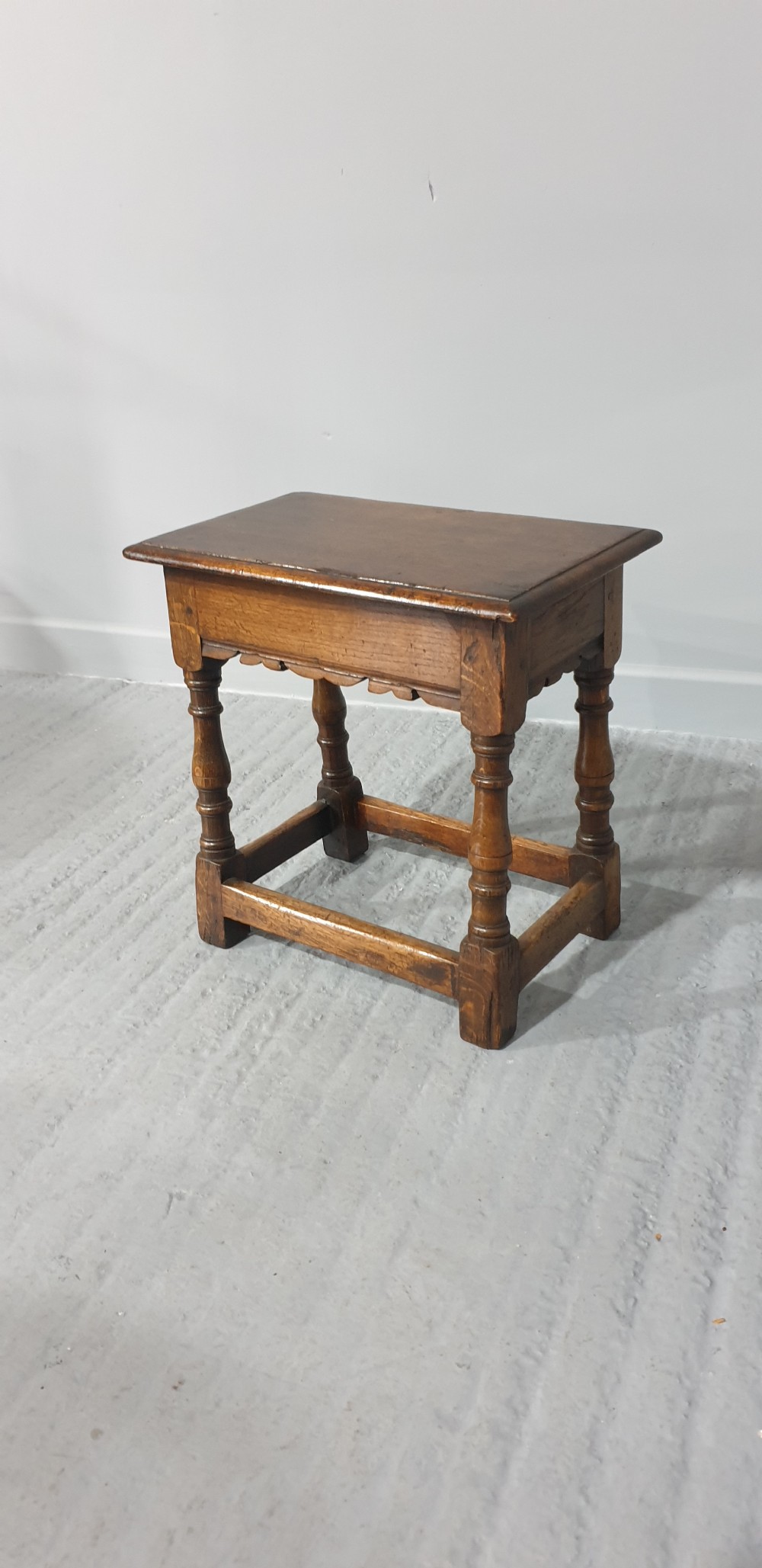 A rectangular oak joint stool featuring turned legs, a shaped apron, and perimeter box stretchers. View III