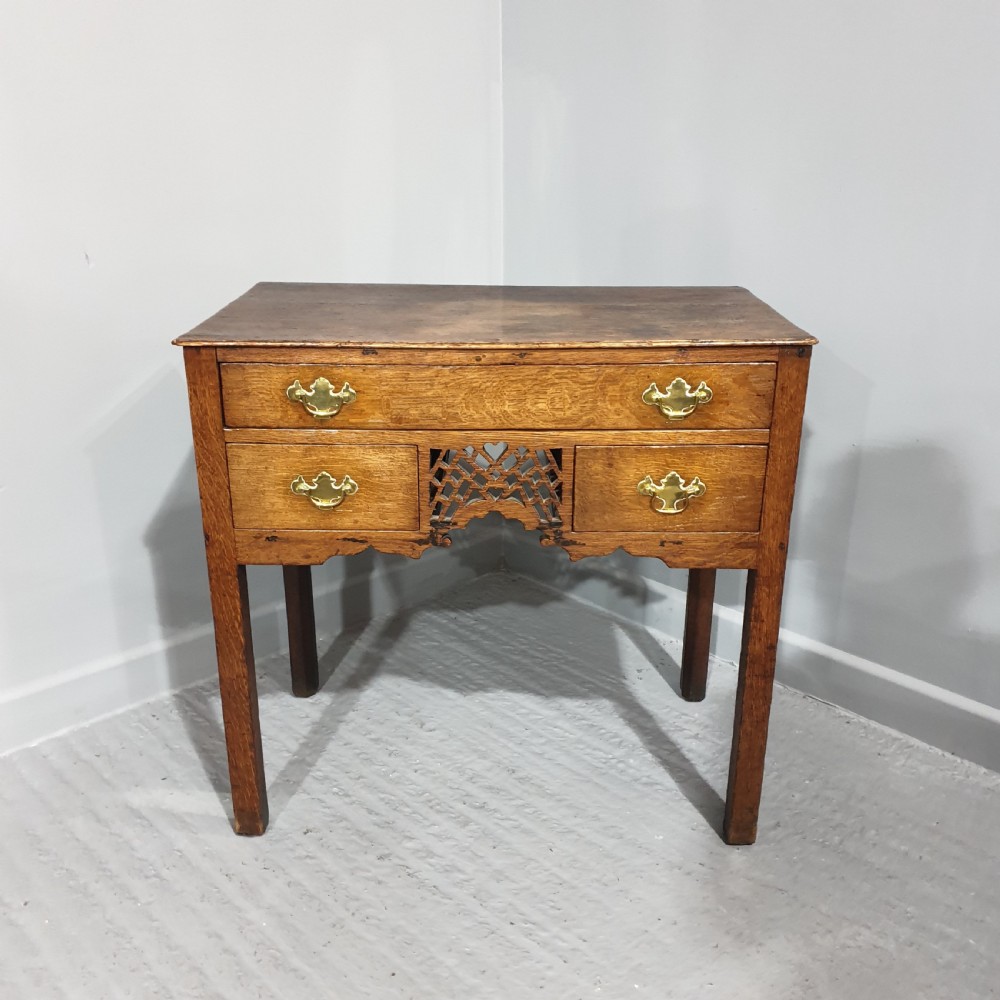 A Georgian oak lowboy featuring three drawers with brass handles, a central carved fretwork apron, and straight square legs.