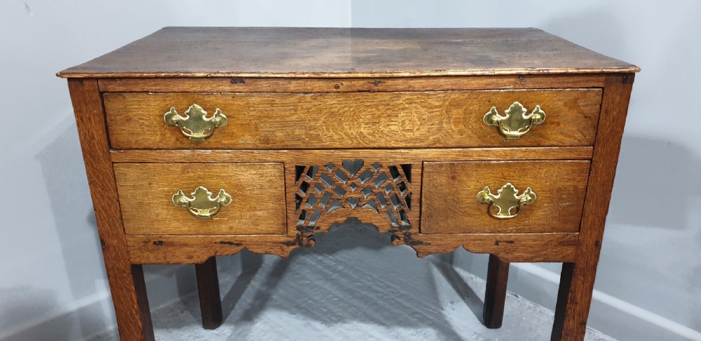 A Georgian oak lowboy featuring three drawers with brass handles, a central carved fretwork apron, and straight square legs. View II