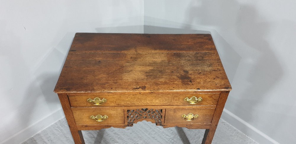 A Georgian oak lowboy featuring three drawers with brass handles, a central carved fretwork apron, and straight square legs. View V