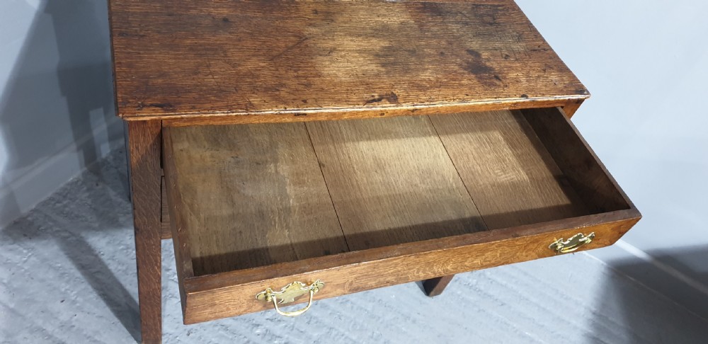 A Georgian oak lowboy featuring three drawers with brass handles, a central carved fretwork apron, and straight square legs. View VII