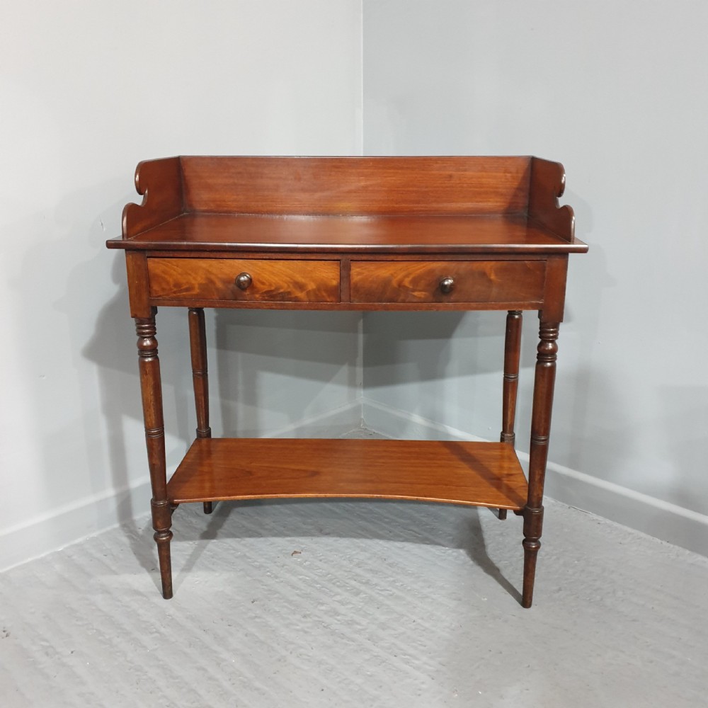 An antique mahogany side table featuring a raised gallery splashback, two frieze drawers with wooden knobs, turned legs, and a lower curved shelf.