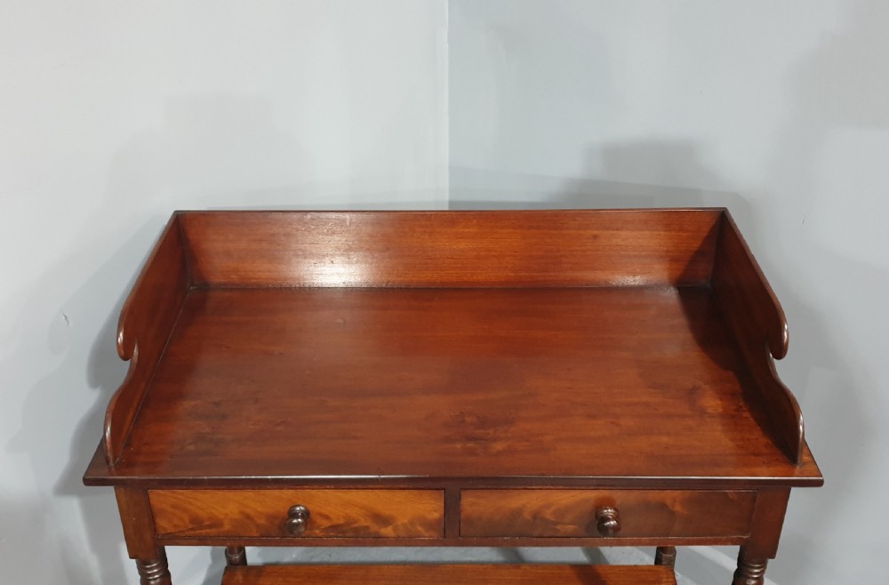 An antique mahogany side table featuring a raised gallery splashback, two frieze drawers with wooden knobs, turned legs, and a lower curved shelf. View V