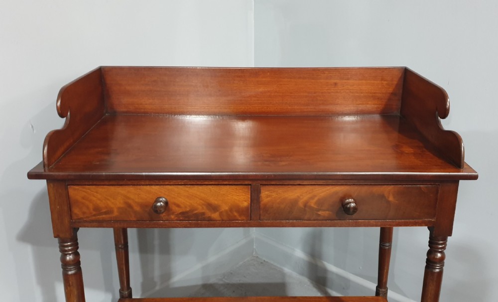 An antique mahogany side table featuring a raised gallery splashback, two frieze drawers with wooden knobs, turned legs, and a lower curved shelf. View VI