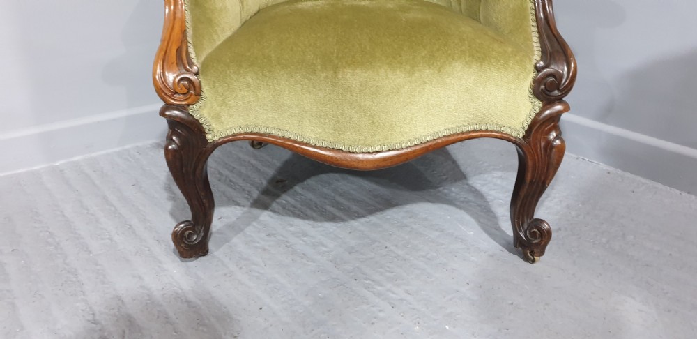 A Victorian library armchair with deep button-tufted olive green velvet upholstery, a carved mahogany frame, and cabriole legs on brass castors. View III
