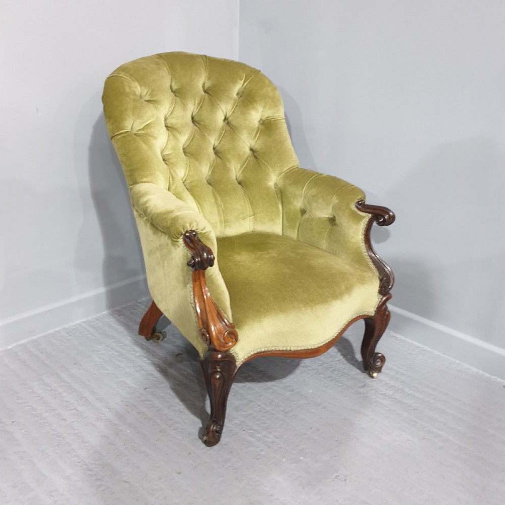 A Victorian library armchair with deep button-tufted olive green velvet upholstery, a carved mahogany frame, and cabriole legs on brass castors. View IV