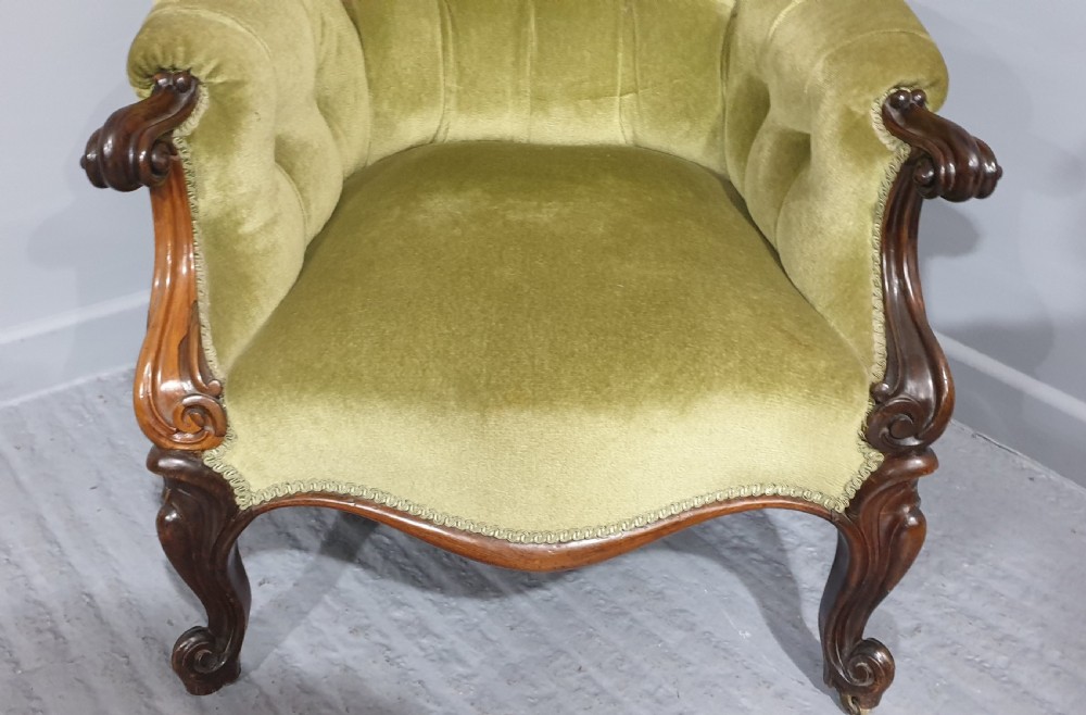 A Victorian library armchair with deep button-tufted olive green velvet upholstery, a carved mahogany frame, and cabriole legs on brass castors. View VI