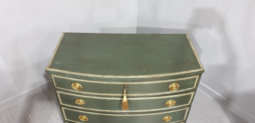 A Georgian green painted bowfront chest of drawers featuring four graduated drawers with cream painted border lines and brass oval drop handles. View VI