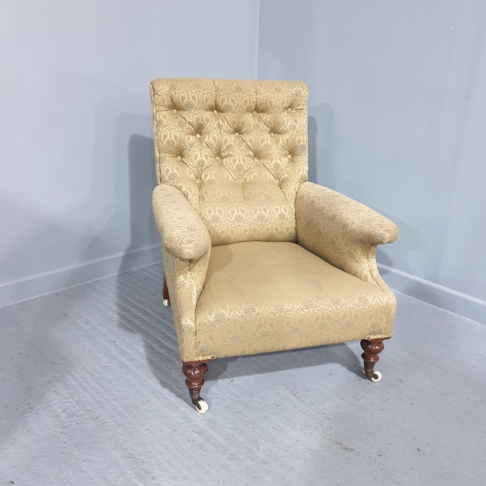 A Victorian library armchair upholstered in gold damask fabric featuring button-back tufting and turned mahogany legs with ceramic castors.