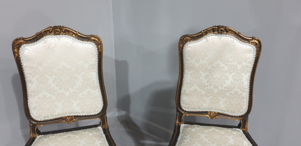 A pair of French Rococo style side chairs with dark ebonised and giltwood frames, carved cabriole legs, and cream damask upholstery. View II