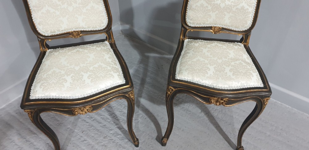 A pair of French Rococo style side chairs with dark ebonised and giltwood frames, carved cabriole legs, and cream damask upholstery. View III