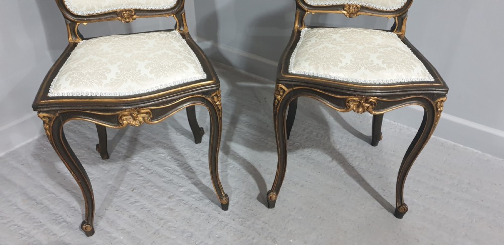 A pair of French Rococo style side chairs with dark ebonised and giltwood frames, carved cabriole legs, and cream damask upholstery. View IV