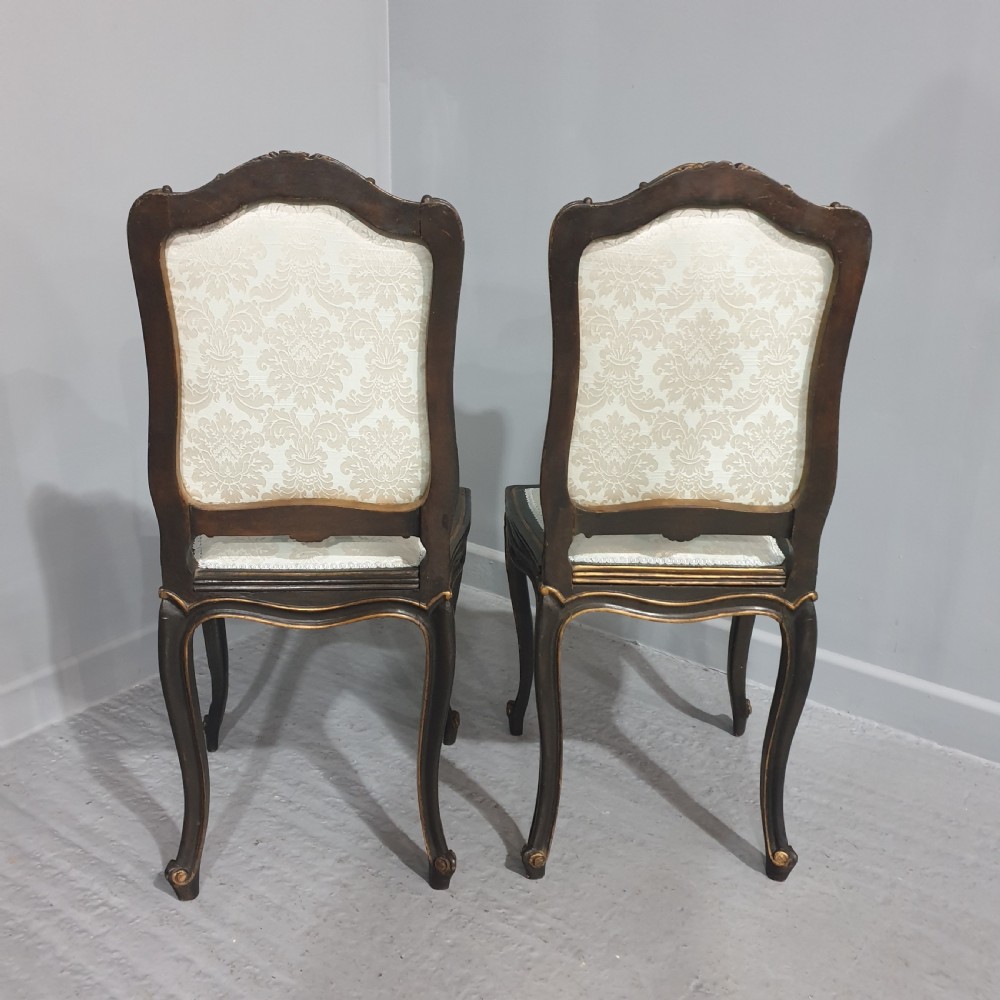 A pair of French Rococo style side chairs with dark ebonised and giltwood frames, carved cabriole legs, and cream damask upholstery. View VI