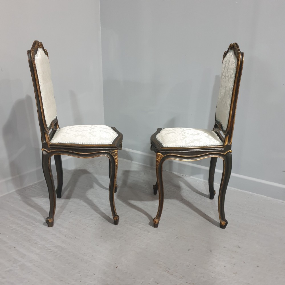 A pair of French Rococo style side chairs with dark ebonised and giltwood frames, carved cabriole legs, and cream damask upholstery. View VII