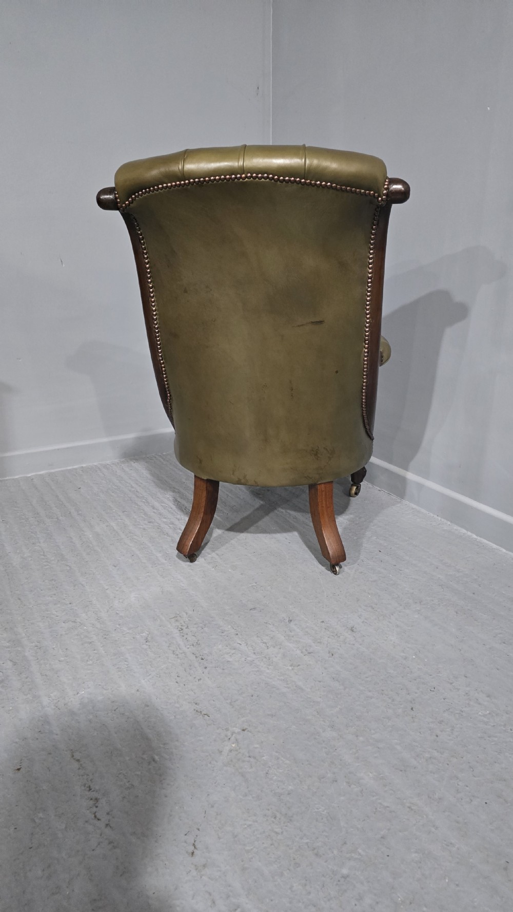 An antique Victorian green leather library chair with deep-buttoned upholstery, carved mahogany frame, scrolled arms, and cabriole front legs on brass castors. View IV