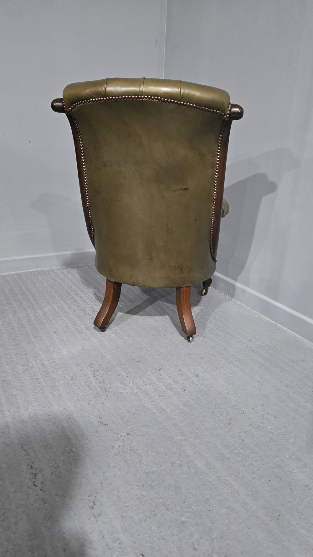 An antique Victorian green leather library chair with deep-buttoned upholstery, carved mahogany frame, scrolled arms, and cabriole front legs on brass castors. View V