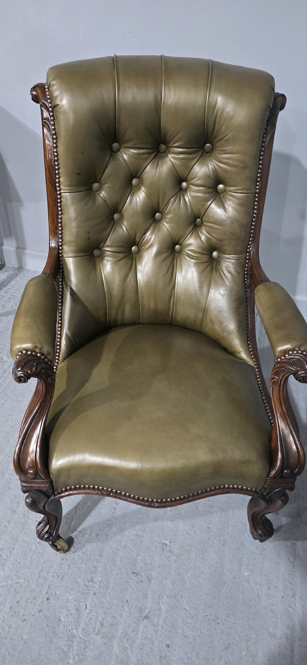 An antique Victorian green leather library chair with deep-buttoned upholstery, carved mahogany frame, scrolled arms, and cabriole front legs on brass castors. View VIII