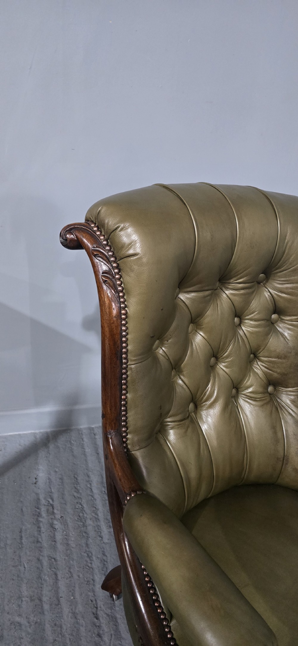 An antique Victorian green leather library chair with deep-buttoned upholstery, carved mahogany frame, scrolled arms, and cabriole front legs on brass castors. View IX