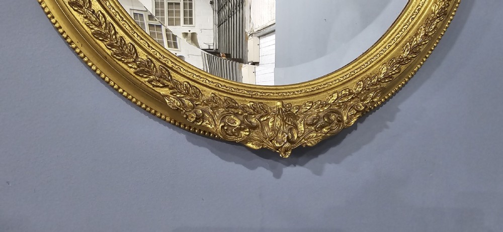 A matching pair of oval giltwood wall mirrors featuring ornate carved top crests and decorative inner rims. View III