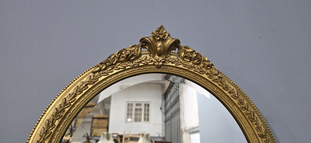 A matching pair of oval giltwood wall mirrors featuring ornate carved top crests and decorative inner rims. View V