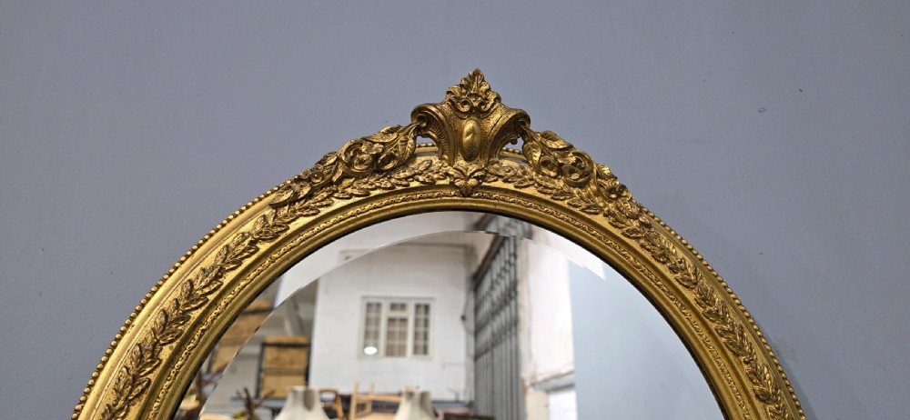 A matching pair of oval giltwood wall mirrors featuring ornate carved top crests and decorative inner rims. View VI