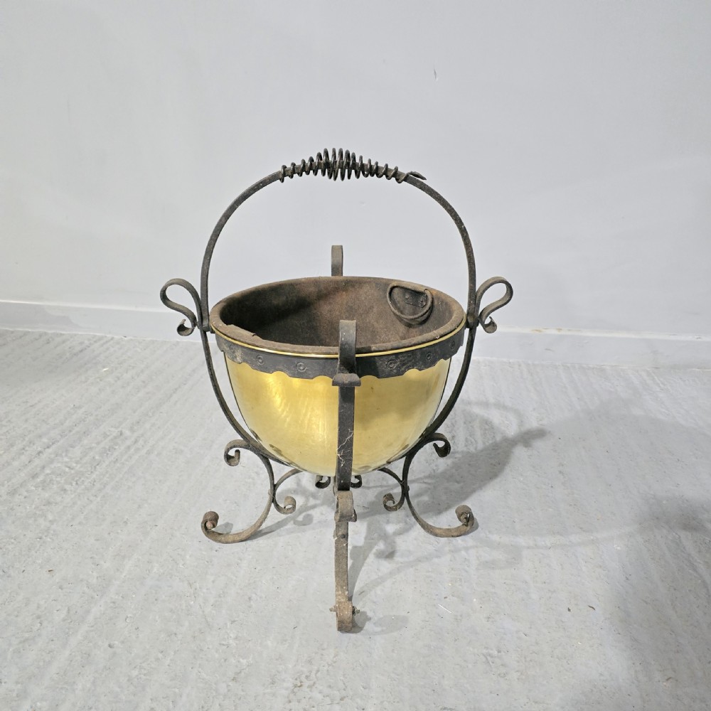 An Arts and Crafts coal bucket featuring a hemispherical brass bowl set within a wrought iron frame with scrolled feet and a spiral wire handle. View II