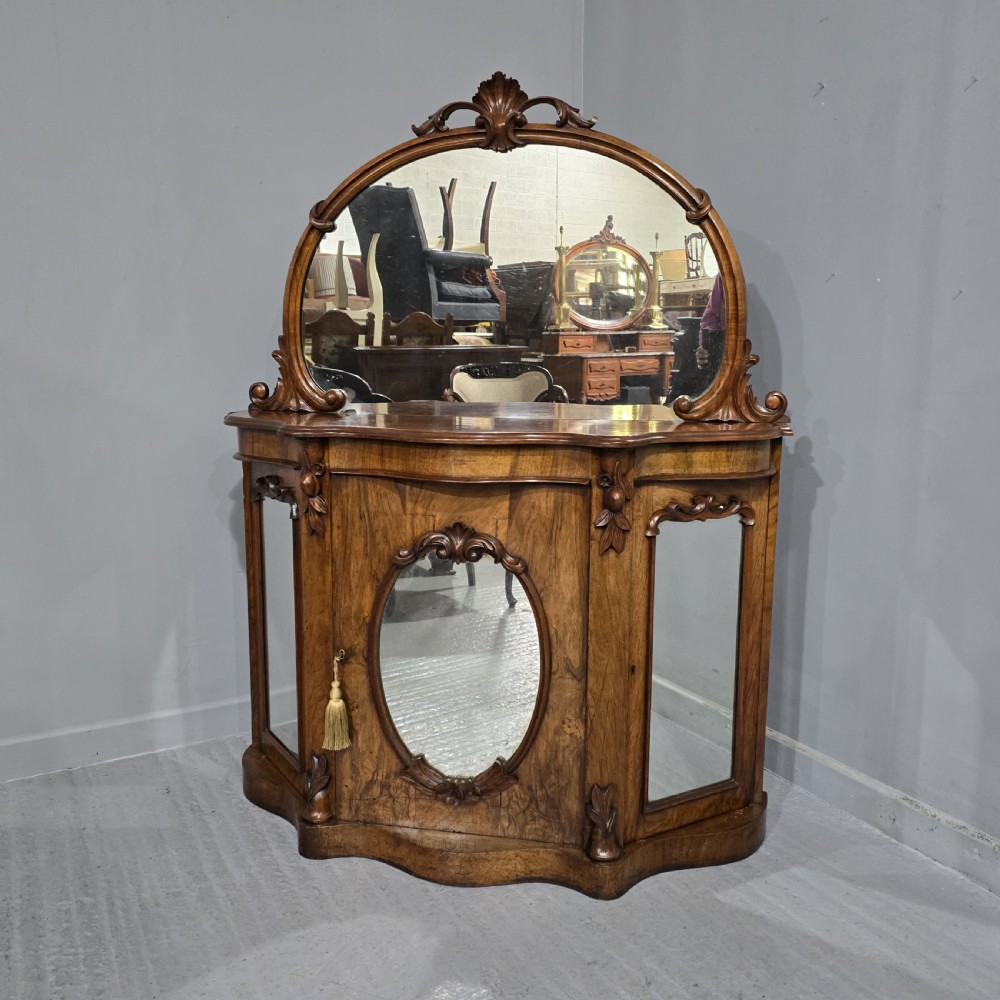 An antique burr walnut side cabinet featuring an arched top mirror with a carved cresting and glass mirrored door panels.